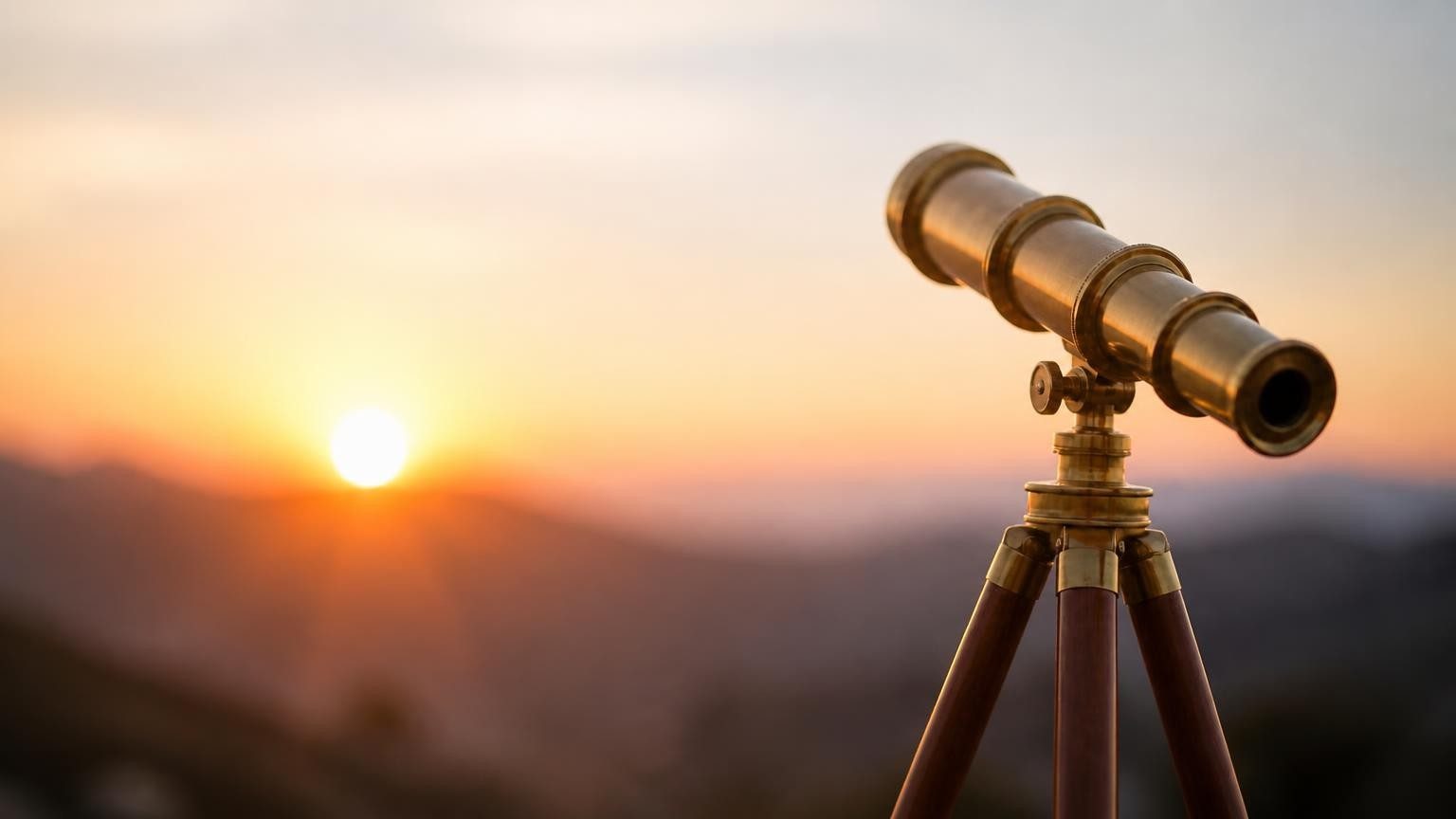 A brass telescope on a tripod overlooking a valley at sunrise.